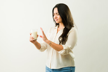 Lactose-intolerant hispanic woman grimacing, pushing away milk glass, expressing dairy product...