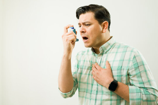 Man using an inhaler during an asthma attack, experiencing breathing problems and chest pain