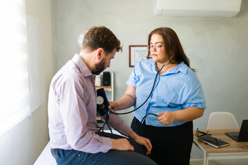 Fototapeta premium Focused female doctor checking blood pressure of a male patient during medical consultation in doctor's office