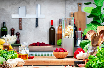 Healthy vegan eating, drinking, cooking, food blogging background with blender with bananas, raspberries and vegan milk for smoothies on wooden board on cozy kitchen with wooden table, kitchenware