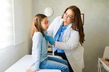 Female doctor using stethoscope examining girl's chest during medical consultation in doctor's...