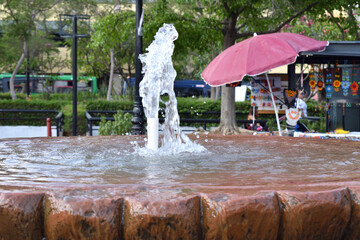 Zapopan, Mexico - June 8 2024: Detailed view of a stone fountain with flowing water in a public square in downtown Zapopan, with a street vendor in the background