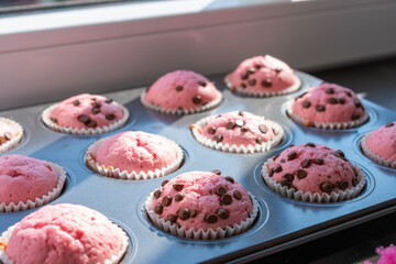 Tray of pink muffins with chocolate chips. The muffins are in paper cups and muffins pan.