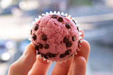 Person is holding pink muffin with chocolate chips. The muffin is in a paper wrapper