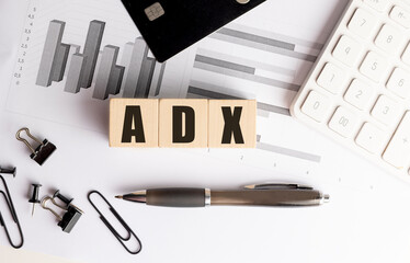 Wooden blocks with abbreviation adx on financial documents with charts, pen, calculator