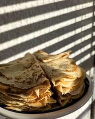Sun through blinds on a white wall, pancakes on a bowl