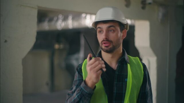 Caucasian technician builder pointing constructor speaking walkie talkie radio architect instruct in construction man foreman waving hand male engineer gesturing control building inspection production