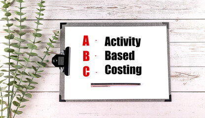Clipboard with text activity based costing abbreviation on white wooden desk with pen and...
