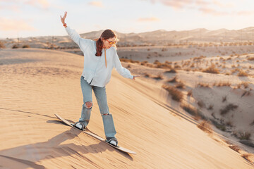 Tourist sandboarding down a sunlit dune in the desert, embracing the thrill and joy of adventure...