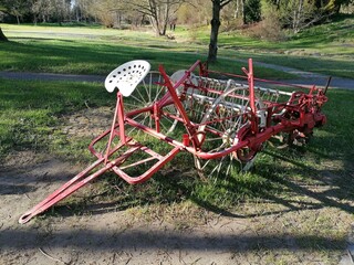 A rustic metal farming implement with a seat in front, likely an antique seed drill. The aged metal and unique design reflect traditional agricultural tools.