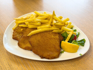 Crispy schnitzel with fries and fresh salad on white plate