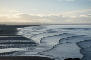 Serene Aberlady Bay in East Lothian, Scotland, showcasing gentle winter waves cascading across wet sand at low tide, bordered by soft cloudy skies on a tranquil coastal morning - Seton Sands, UK
