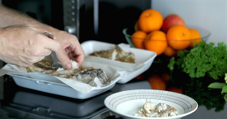 Hands seasoning baked fish with fresh oranges, parsley on black countertop, culinary preparation, home cooking, healthy meal concept.