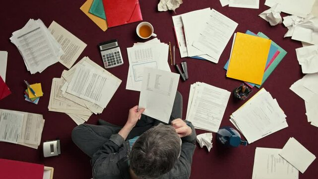 Accounting and processing a mess of paperwork. Man doing challenging work with taxes, overhead spinning shot
