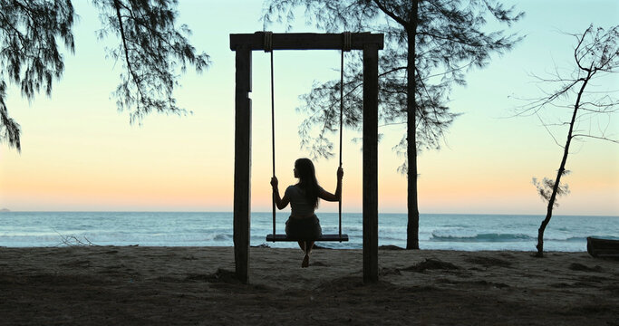 Silhouette of woman on swing at beach during sunset.