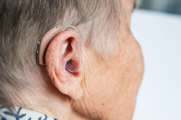 Naklejka premium Close-up of an elderly woman’s ear with a hearing aid, symbolizing age-related hearing loss, assistive technology, and senior healthcare.