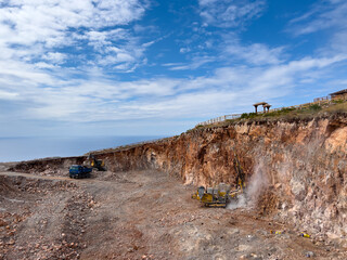 Drilling rigs work in a quarry against a cloudy sky