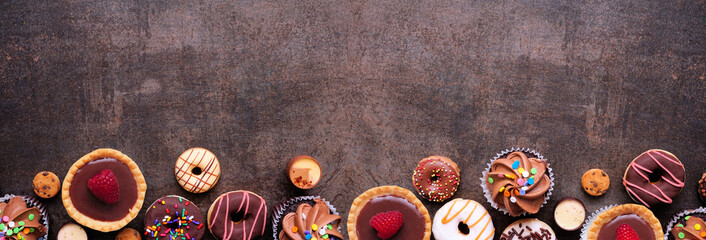 Dessert bottom border with a collection of sweets. Top view on a dark stone banner background with copy space.