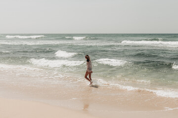 A surfer girl in a black swimsuit walks along the shoreline with her shortboard, sips fresh coconut, and relaxes under palm trees. A perfect blend of surfing, tropical vibes, and beachside escape