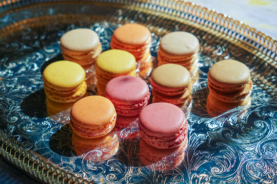 Macaroons of different colors with different flavors and pearl beads on the golden metal tray. Sweet treats for guests to the wedding or party.