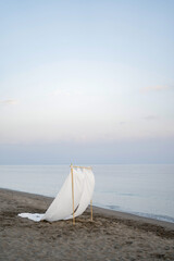 Wedding arch with fluttering white sheets stands on a sandy beach by the sea