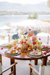 Festive table with bright flowers and plates on wicker mats stands on the restaurant terrace overlooking the sea
