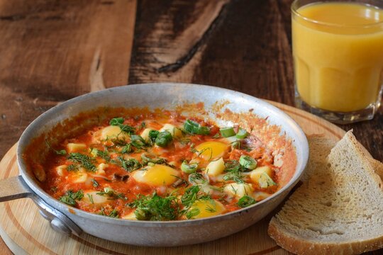 Breakfast shakshuka in frying pan with glass of orange jouce on wooden board table