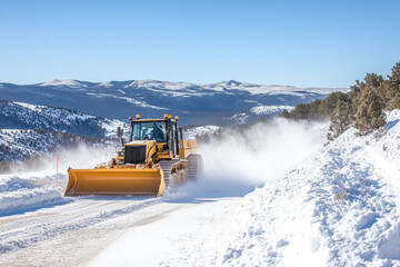Dozer clearing heavy snow from a mountain road, making it passable for vehicles