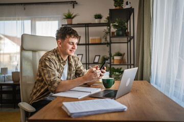young man student study for exam from notes and mobile phone at home