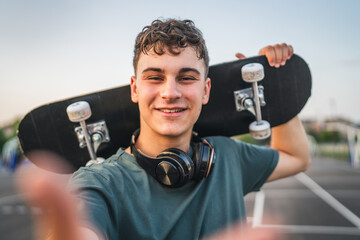 One man young adult caucasian teenager stand outdoor with skateboard on his shoulder and headphones...
