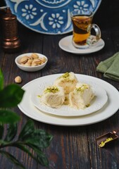 Eastern sweet, pishmaniye or cotton halva with pistachios on a white plate on a dark wooden background. Sweets from around the world.