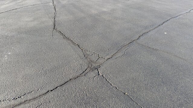overhead view of dark gray asphalt parking surface with white painted lines cracks and worn textures empty spaces clean layout street shadows minimal urban detail captured from above