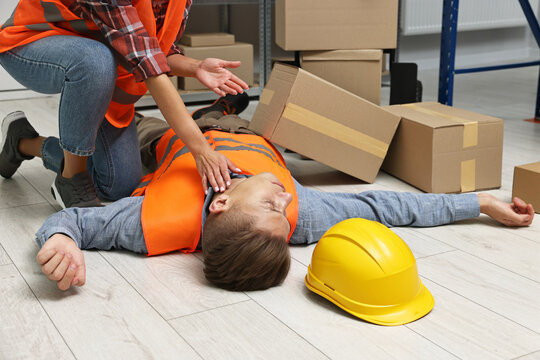 Accident at work. Woman checking pulse of her unconscious colleague in warehouse - Powered by Adobe