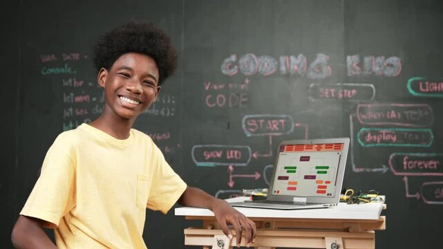 Smart african boy use laptop to code program and turn around to wave hand. Cute high school stident coding engineering prompt or program system at blackboard in STEM technology classroom. Edification