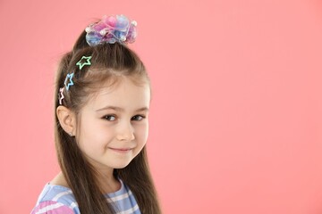 Happy little girl wearing beautiful hair accessories on pink background, space for text
