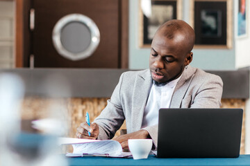 Obraz premium Head shot serious puzzled African American businessman looking at laptop screen sitting in office. Executive managing thinking received bad news keeping fist at chin waiting hoping positive result.