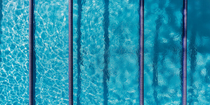 Aerial view of turquoise swimming pool lanes, showing textured water surface and dark lane dividers, representing summer, sport, and aquatic leisure