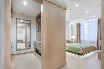 A spacious dressing room with storage space and a passage to a bright bedroom with a modern interior.