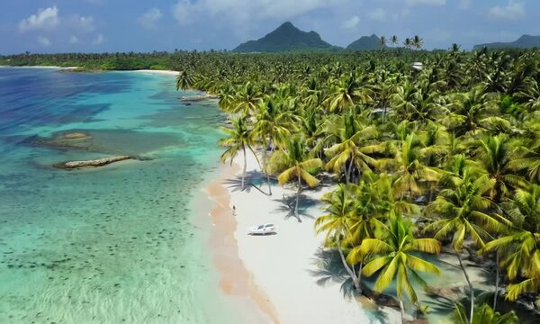 Aerial cinematic drone shot over tropical beach with white sand and palm trees over sea water at tropical paradise. Cinematic nature aerial outdoor, beautiful tropical paradise beach. Camera move left