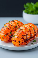 Two grilled lobster tails, seasoned and garnished with parsley, served on a white plate
