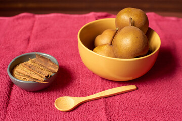 Yellow ceramic bowl brimming with golden pears resting on vibrant fuchsia textured background,...
