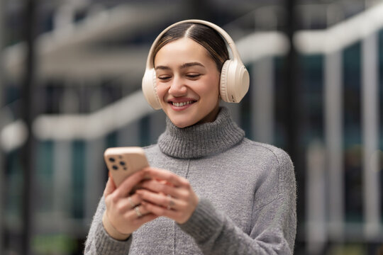 Scrolling, sharing, staying connected. A woman with headphones and smartphone reacts to social media updates, capturing real-time engagement in a world driven by digital connections
