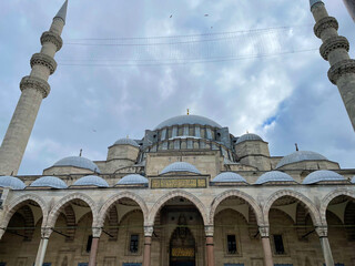 Exterior mosque view showcasing bright turquoise dome and twin minarets beneath light cloud cover A...