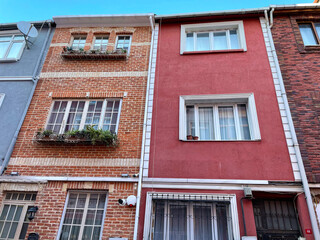 Obraz premium Diverse architectural facades of three adjacent urban buildings under clear blue sky Distinct red, brick, and gray façades showcase urban character with balconies, plants, and bright sky above