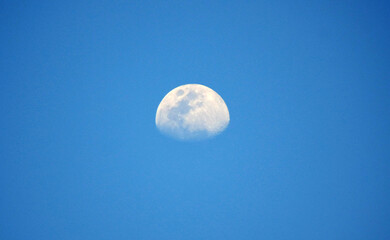 A bright crescent moon glowing beautifully in the daytime against a deep blue sky, creating a...
