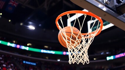 Basketball going through hoop and net in indoor arena with blurred spectators. Successful score concept.