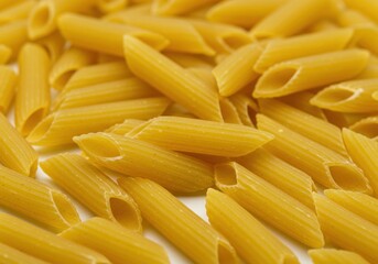 Uncooked penne pasta with vibrant yellow color and ridged texture arranged on a white background
