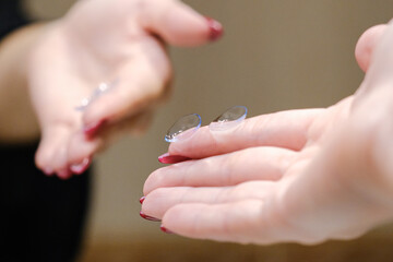A woman’s hand holding contact lenses against a mirror background with a reflection. Health and comfort.