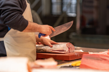 A fishmonger skillfully fillets a fresh fish with a large knife at a seafood market. The scene captures the essence of fresh, healthy, and protein-rich seafood
