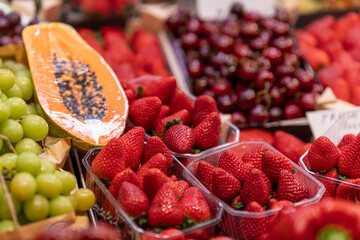 Fresh strawberries, grapes, cherries, and sliced papaya displayed in rustic baskets at a vibrant farmers market, showcasing colorful, organic, and healthy produce.